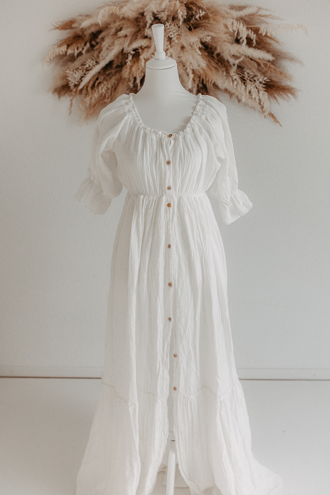 Auf dem Bild sieht man ein weißes Kleid, getragen von einer Schaufensterpuppe und Pampasgras im Hintergrund