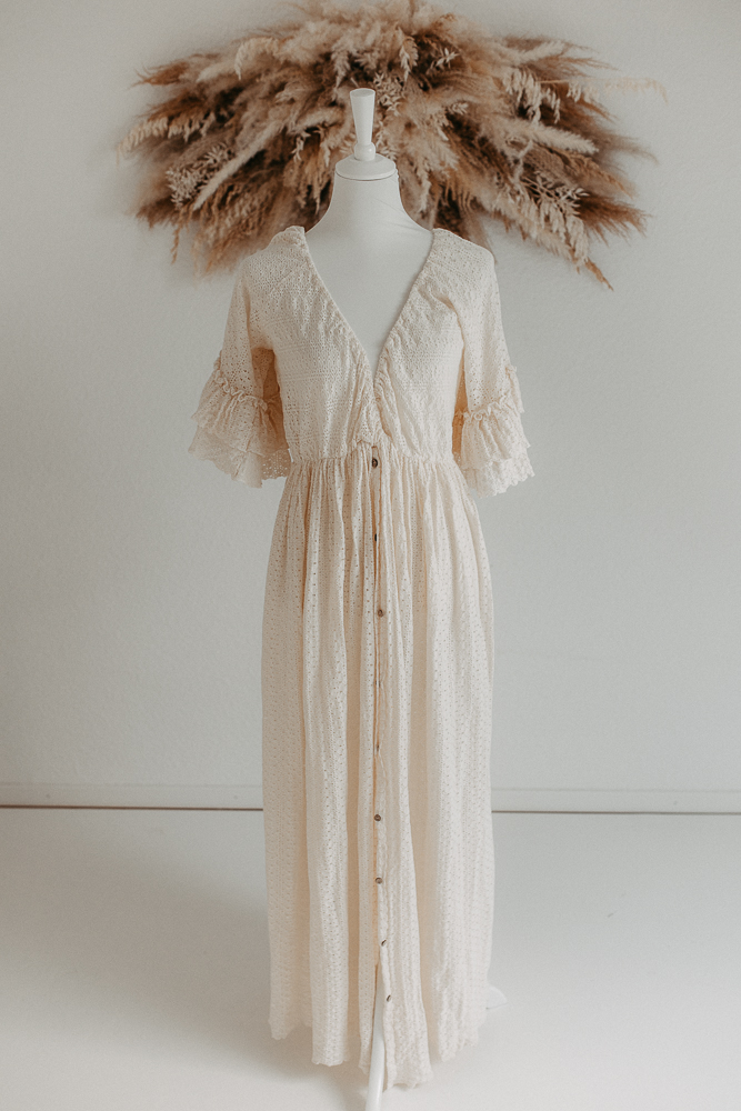 Auf dem Bild sieht man ein beiges Spitzenkleid, getragen von einer Schaufensterpuppe und Pampasgras im Hintergrund