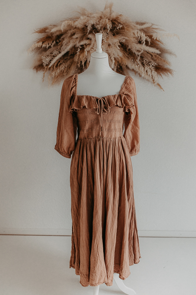 Auf dem Bild sieht man ein braunes Kleid, getragen von einer Schaufensterpuppe und Pampasgras im Hintergrund