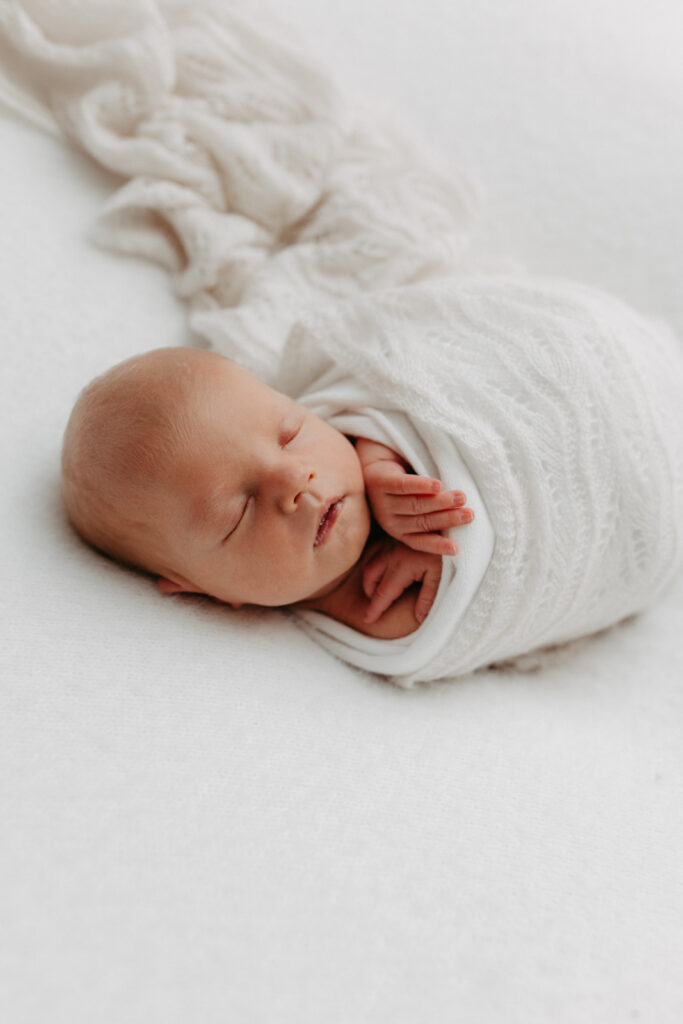 Auf dem Bild sieht man ein Baby, eingepuckt in ein creme farbenes Tuch